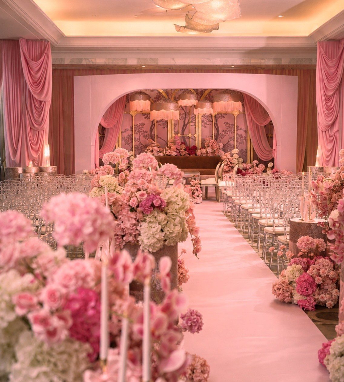 Pink wedding venue with floral arrangements, pink aisle runner, and draped curtains.