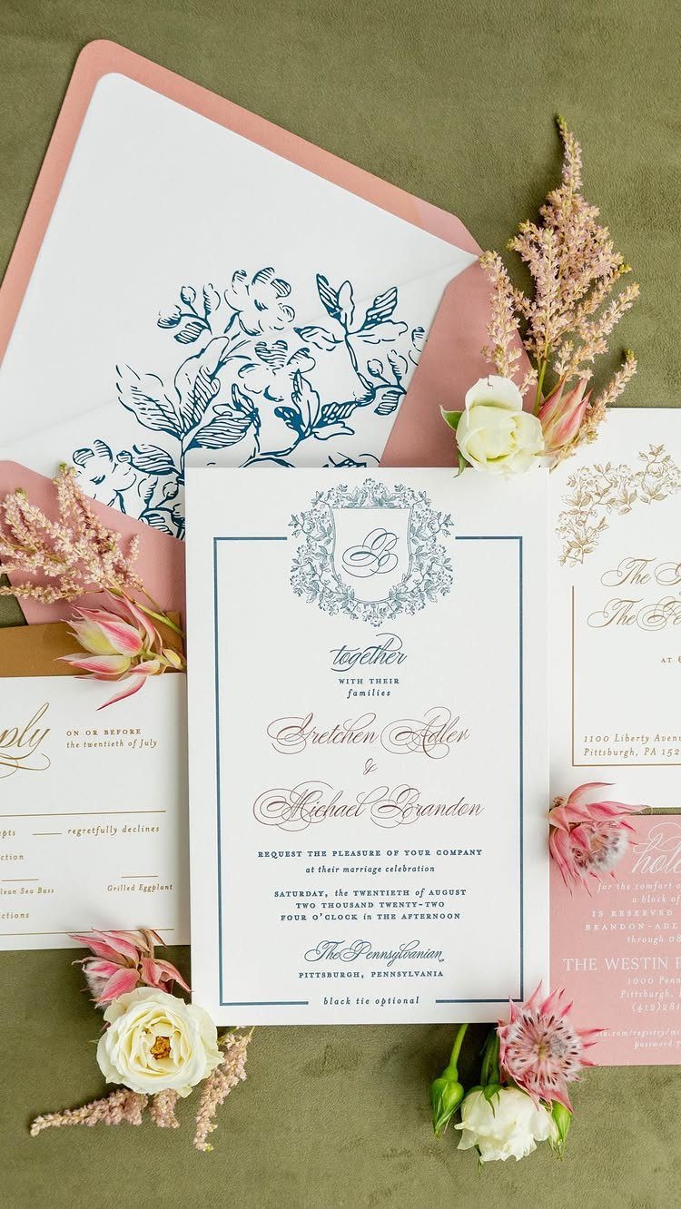 Wedding invitation suite with navy blue text, dusty rose envelope, and pink flowers.