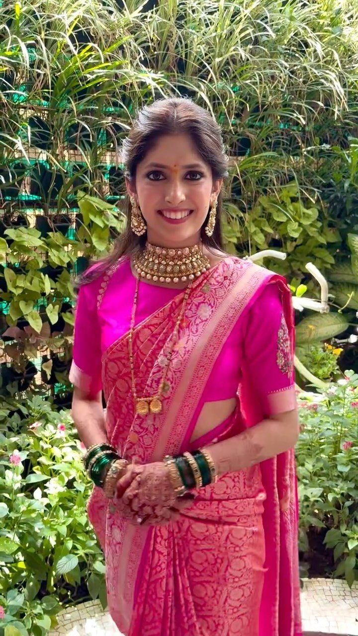 Woman in a vibrant fuchsia pink silk saree with gold jewelry and greenery background