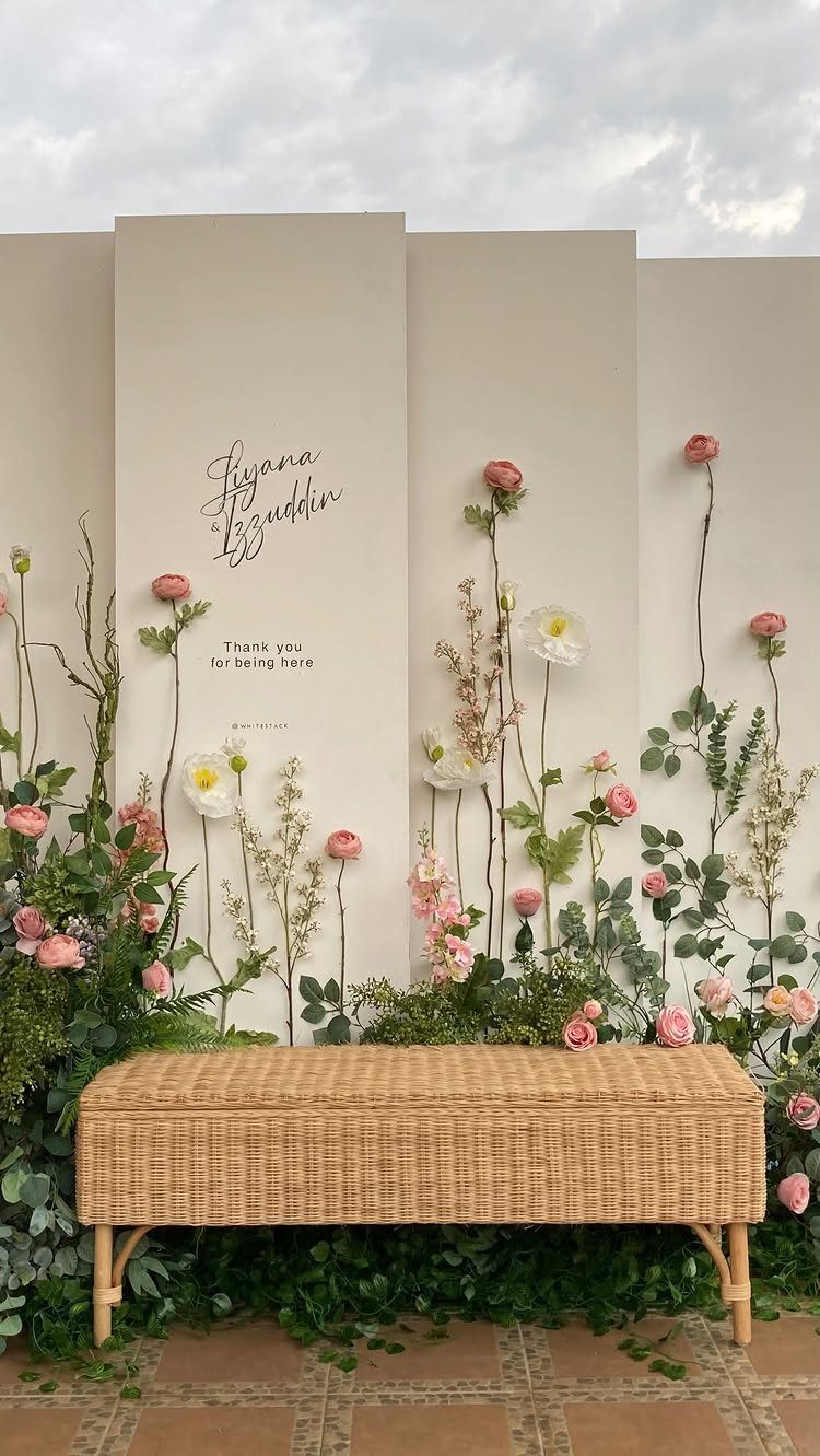 Wedding backdrop with pink roses and white flowers behind a woven wicker bench.
