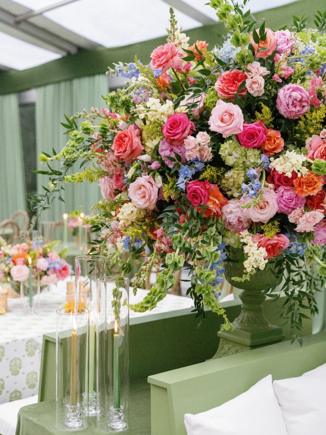 Vibrant floral arrangement with pink, orange, and chartreuse flowers in a green urn.