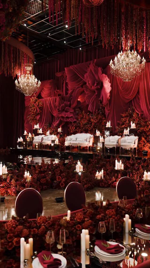 Lavish wedding reception venue decorated in deep red florals and burgundy draped fabrics.