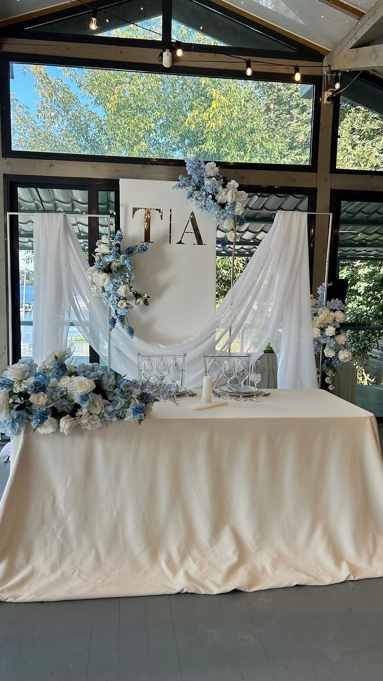 Wedding table with white linens and blue and white floral arrangements and backdrop.