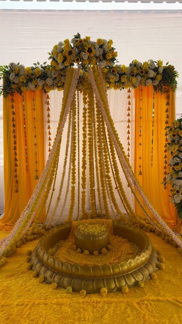 Yellow wedding canopy with floral garlands and golden pedestal on yellow carpet.