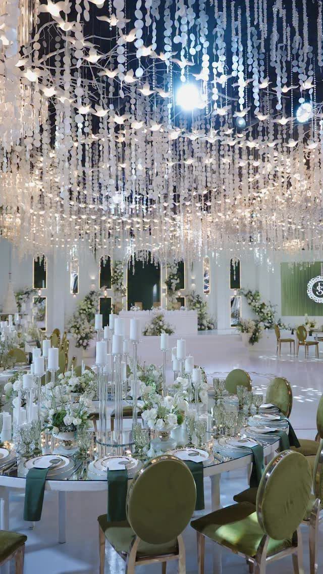 Wedding reception table with white flowers and olive green velvet chairs under crystal ceiling