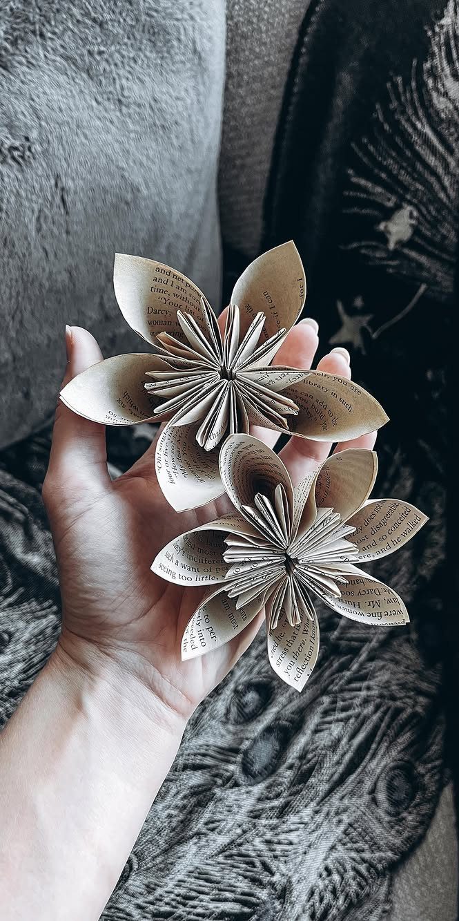 Two handmade flowers made from book pages held in a person's hand.