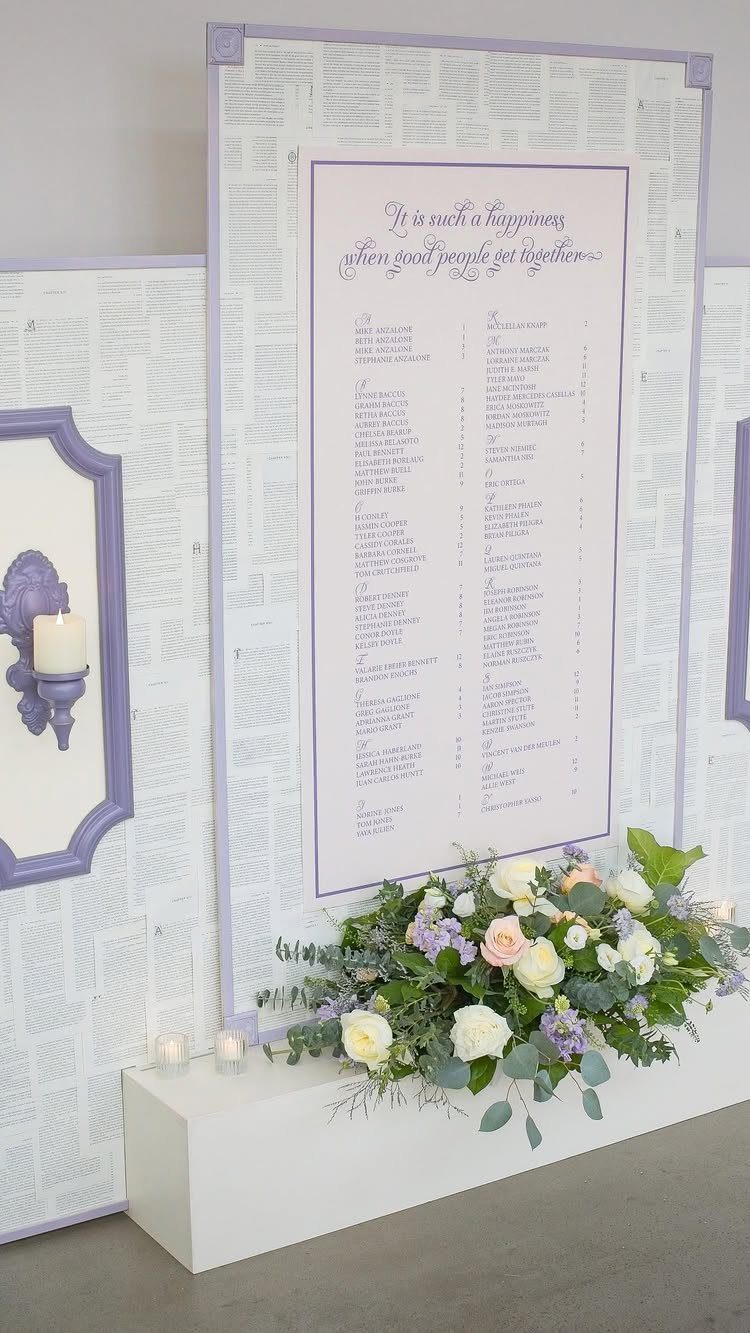 Wedding seating chart with purple borders and floral arrangement on a white plinth