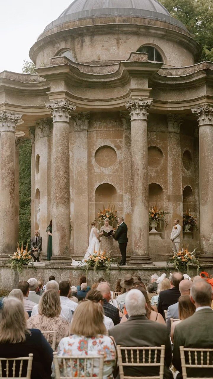 Wedding ceremony held before a classical stone rotunda with guests seated in chairs.