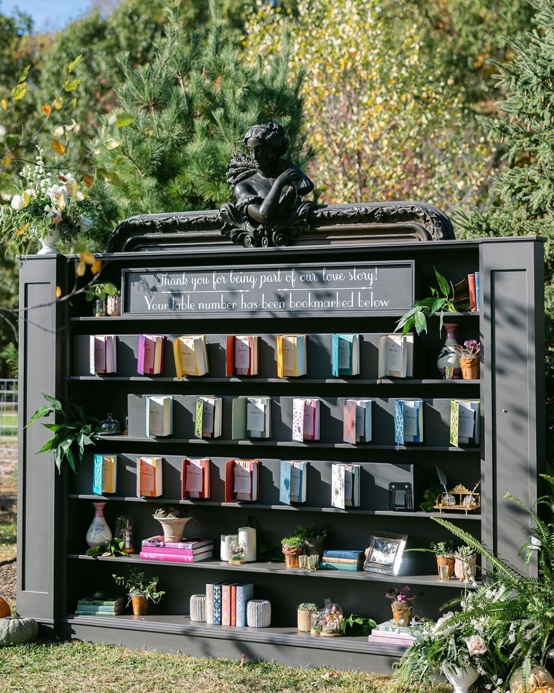 Grey outdoor bookshelf with colorful books used as wedding table number markers.