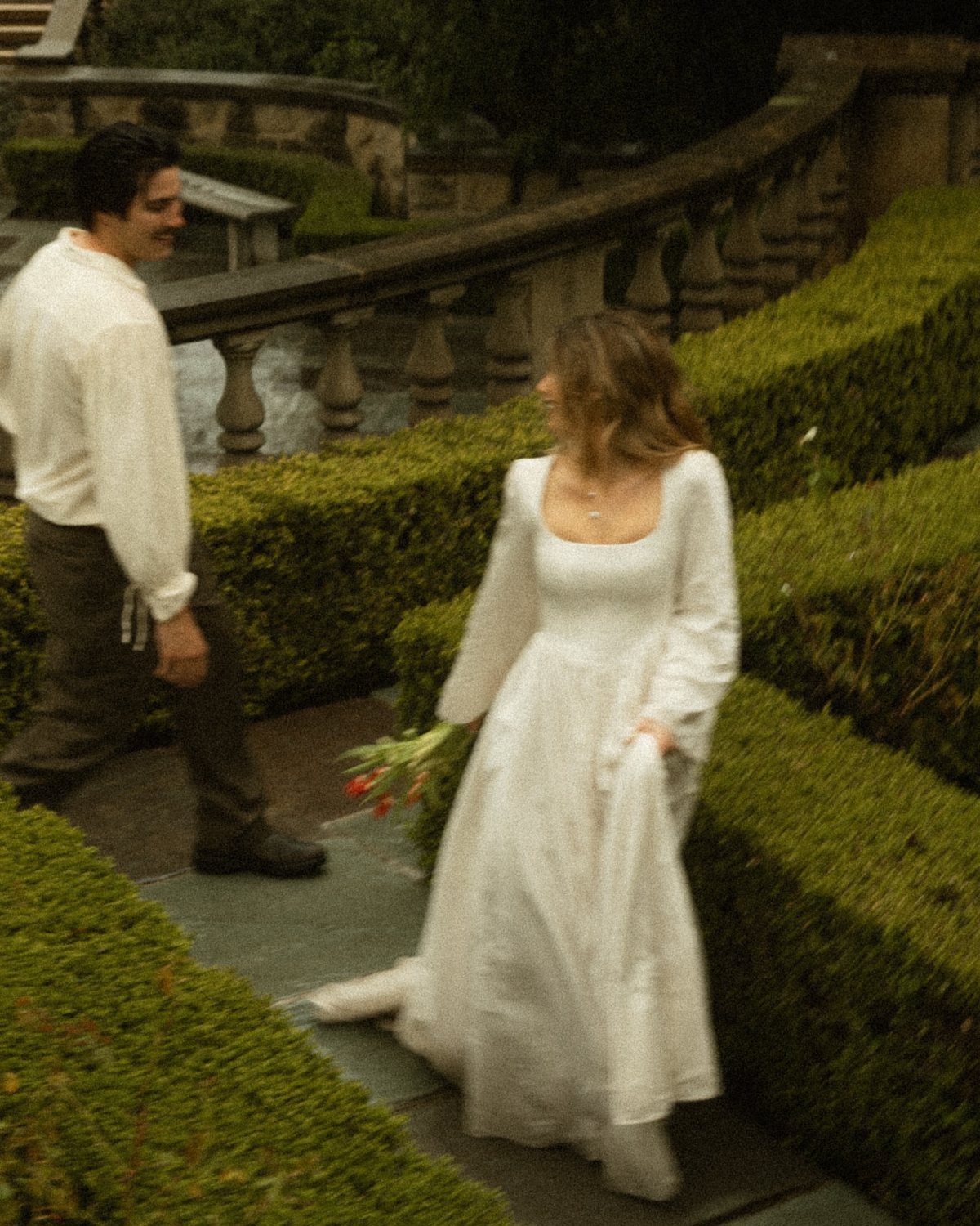 Couple in Regency era attire walking through a formal garden with stone railings
