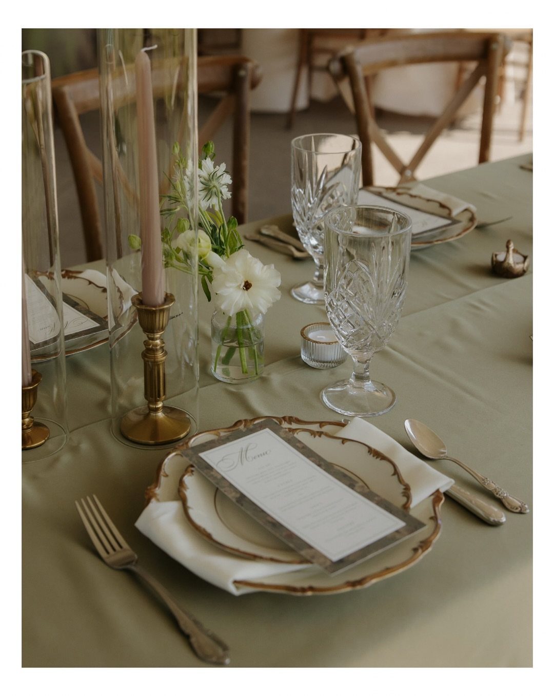 Elegant wedding table setting with sage green linens, gold-rimmed plates, and pink candles.