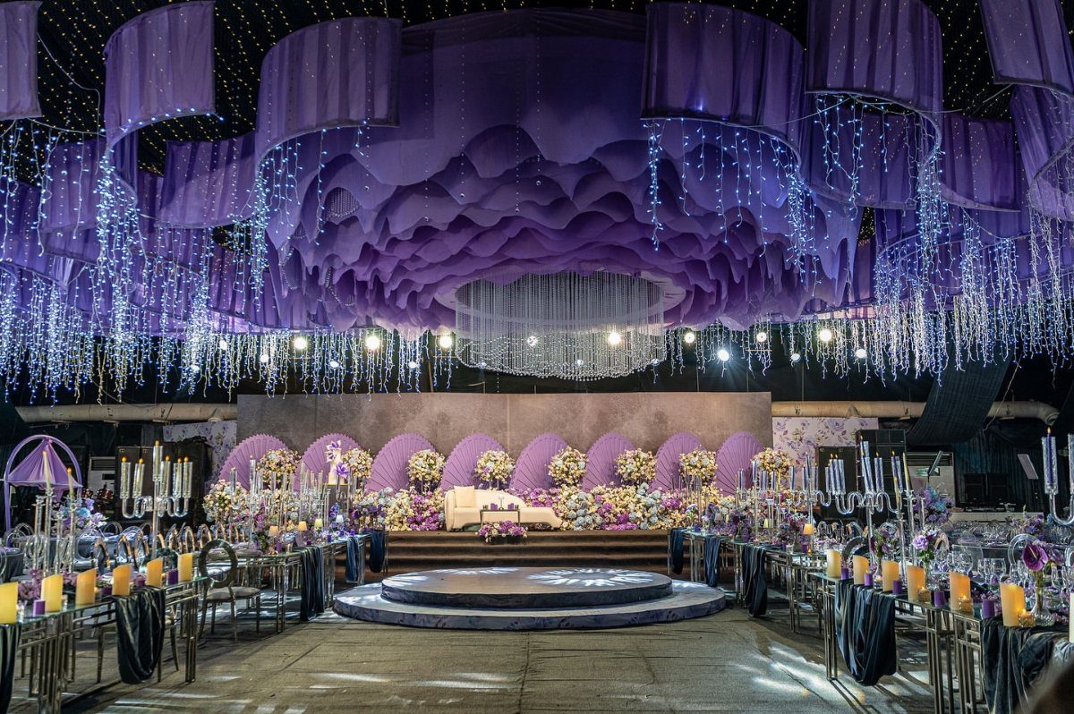 Purple and blue ambient lighting illuminating a wedding venue with draped ceilings and flowers