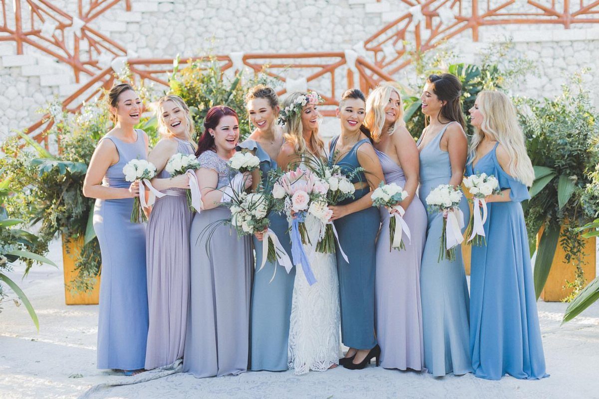 Bridesmaids wearing various shades of blue and purple dresses standing with a bride.