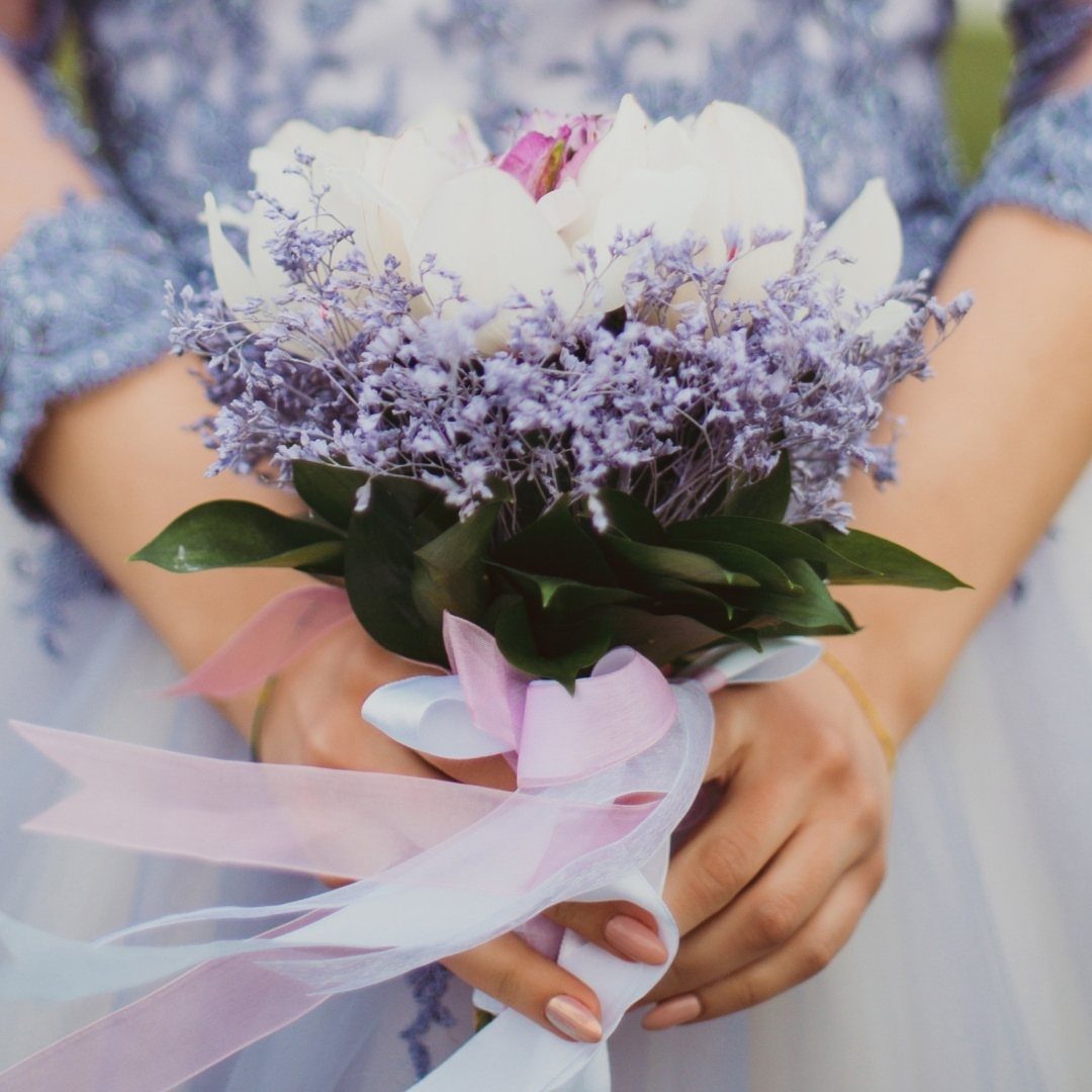 Bouquet of white and purple flowers held by person in blue lace dress