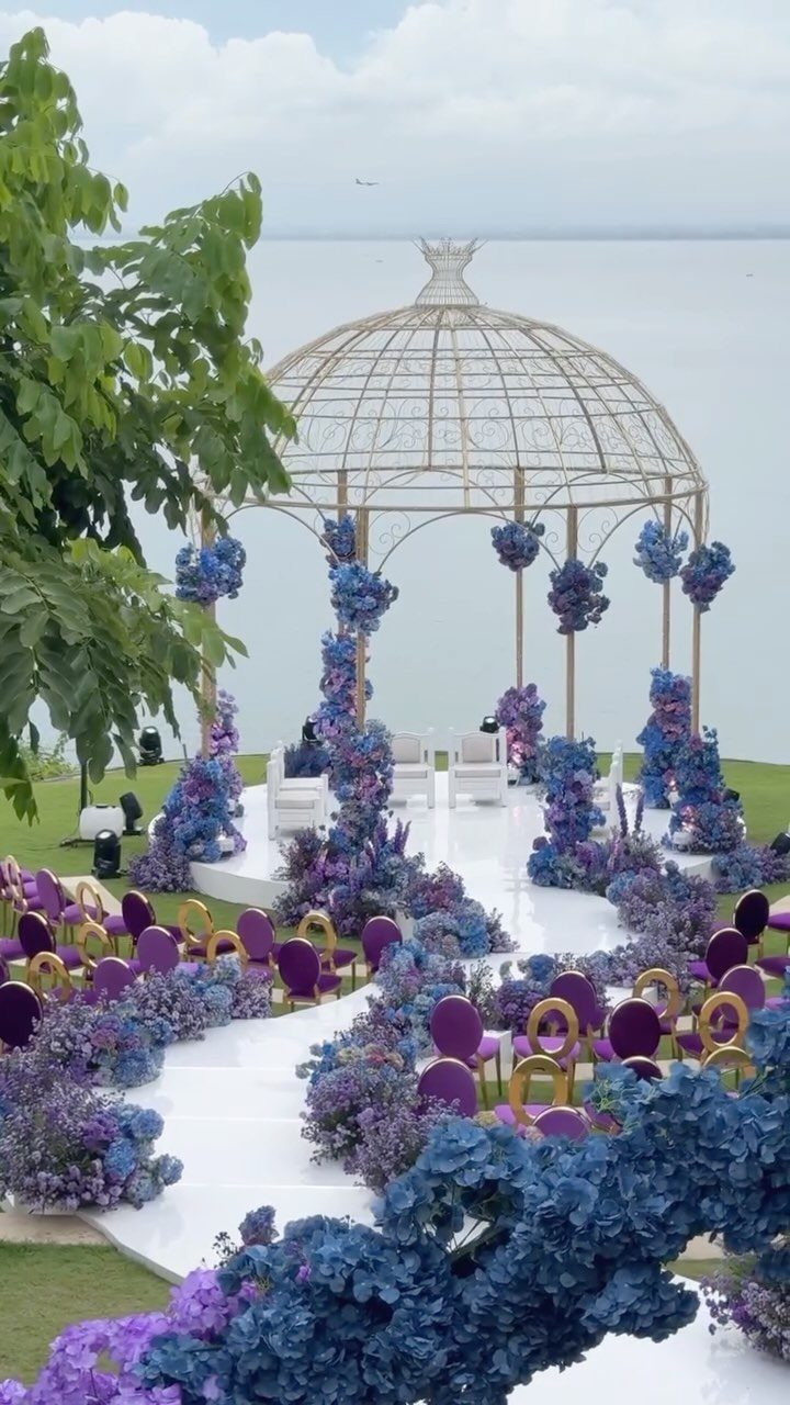 Outdoor wedding ceremony setup with gold gazebo and purple and blue floral decor