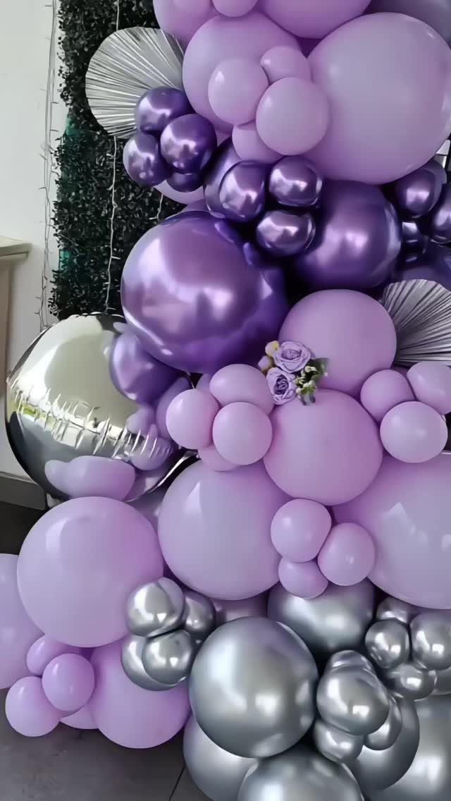 Purple and silver balloon arch with various sizes and metallic finishes against greenery.