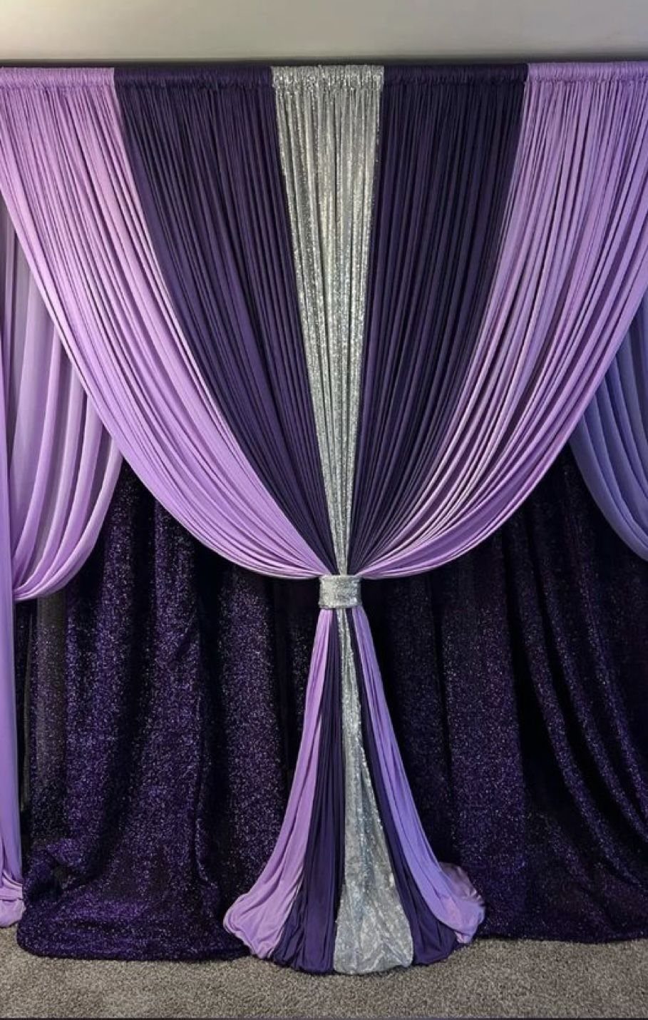 Purple and silver fabric drapes gathered in the center over a sequined backdrop.