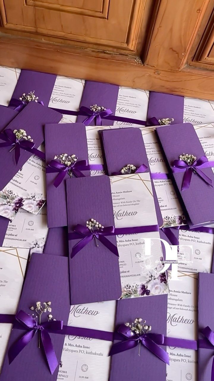 Purple and white wedding invitations tied with purple ribbons and small white flowers.