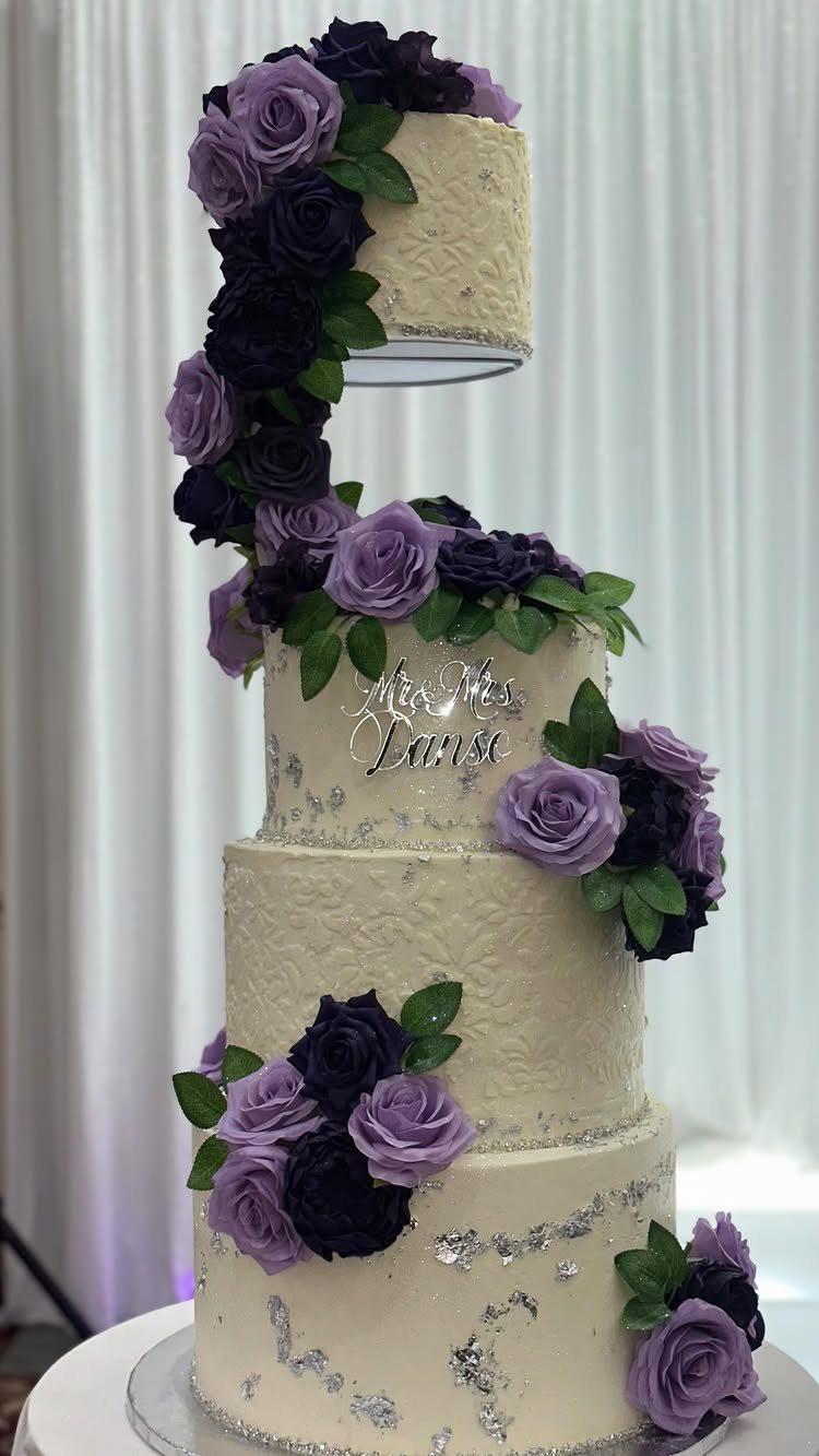 Multi-tiered white wedding cake with purple roses and silver glitter accents