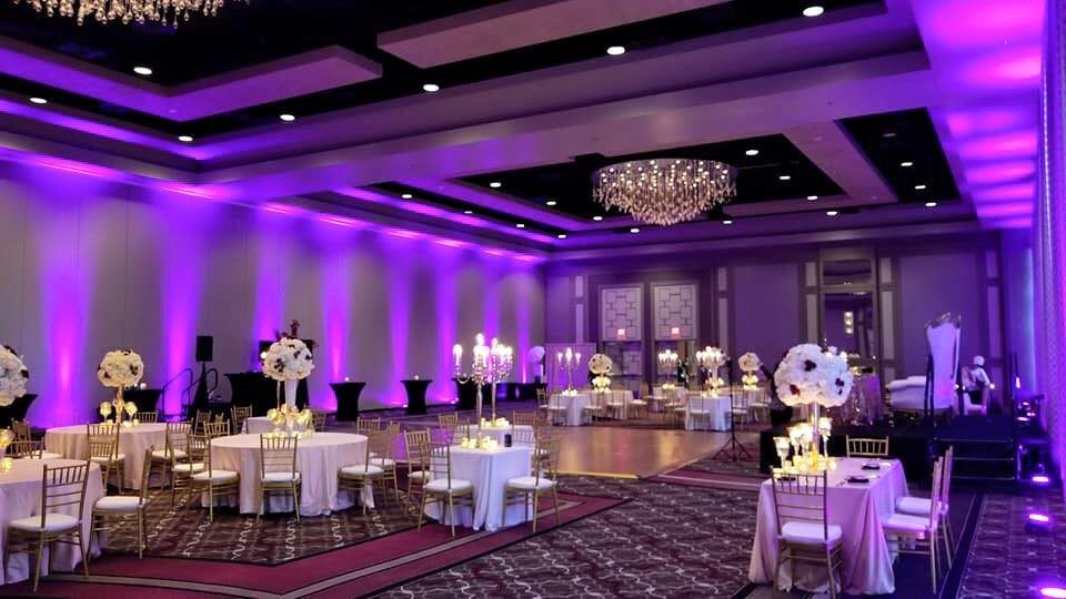 Ballroom wedding reception with vibrant purple uplighting on the walls and white tables.