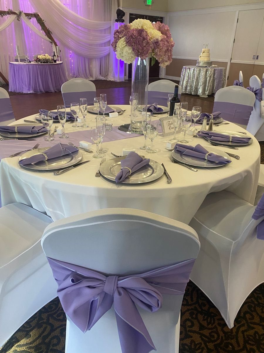 Round wedding table with silver charger plates, purple napkins, and floral centerpiece.