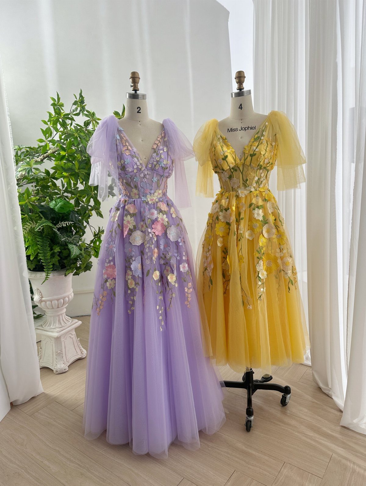 Purple and yellow floral gowns on mannequins in a bright white room.