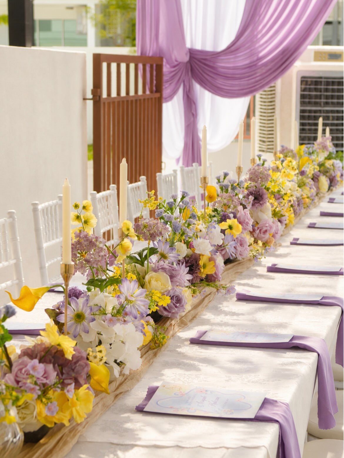 Long white wedding table with purple and yellow floral runner and purple napkins