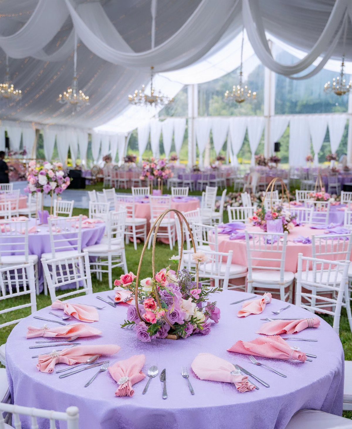 Lilac wedding table settings with pink napkins and floral centerpieces under a white tent.