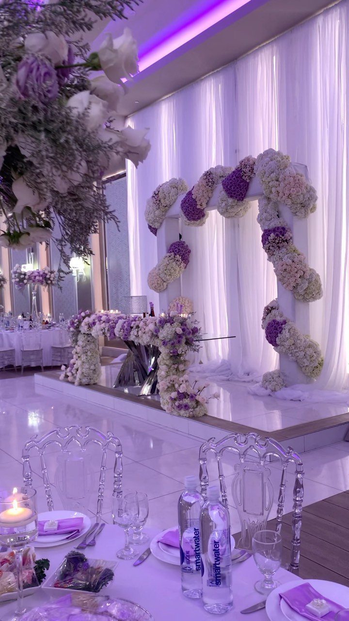 Purple and white floral arrangements decorating a wedding venue with clear acrylic chairs.