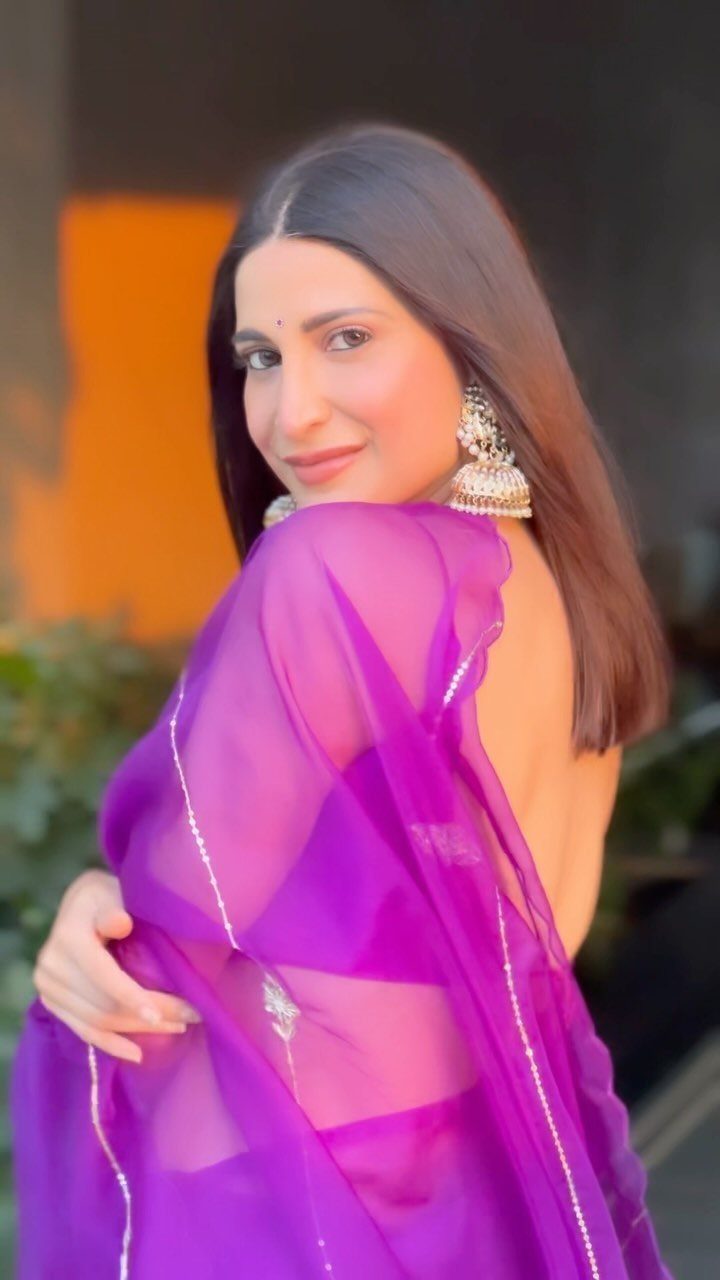 Woman wearing a vibrant purple saree and traditional silver earrings posing outdoors.