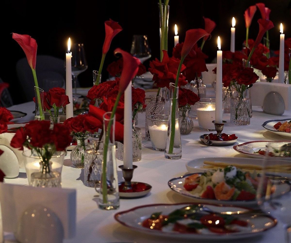 Red roses and calla lilies with white candles on a white wedding table.