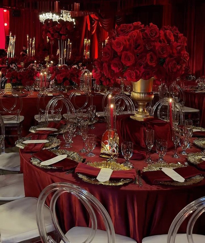 Red satin wedding table setting with gold accents and large red rose centerpieces.