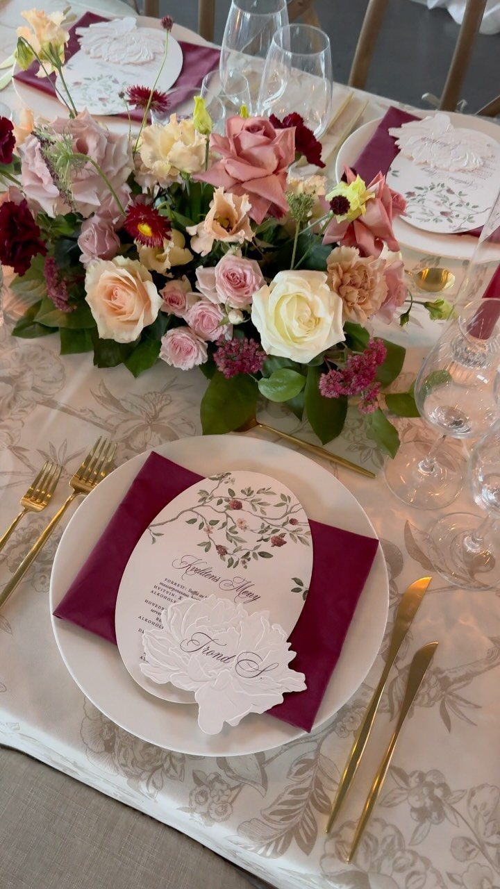 Wedding table setting with red and peach roses, burgundy napkins, and gold cutlery.