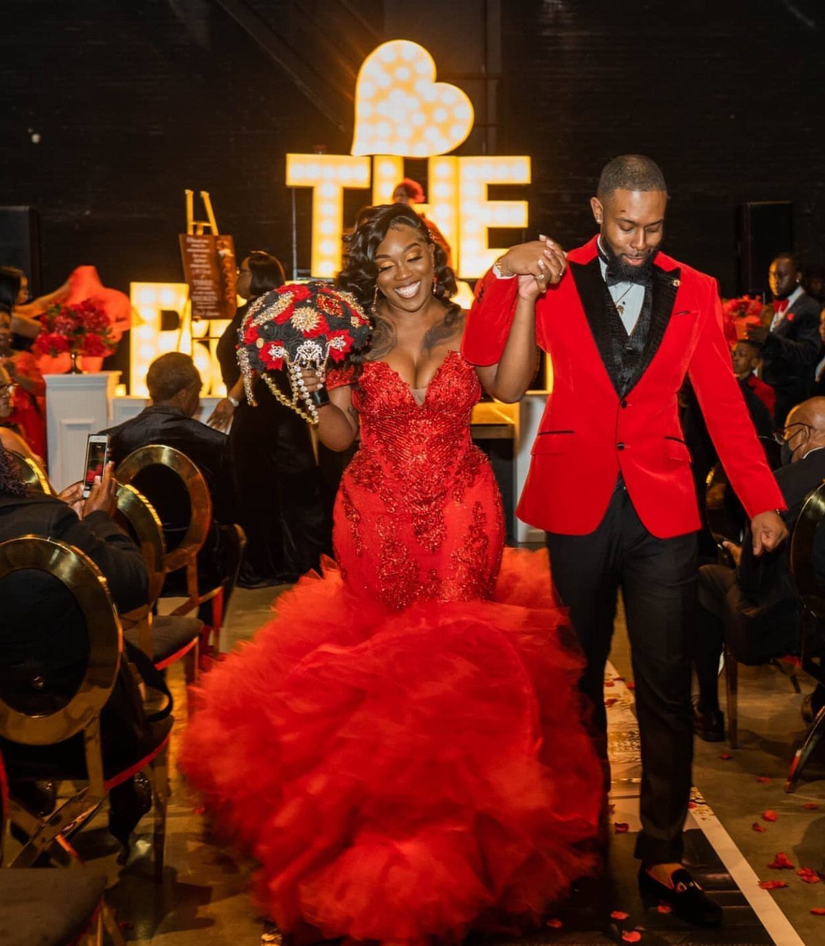 Couple in vibrant red wedding attire walking through a decorated event venue.