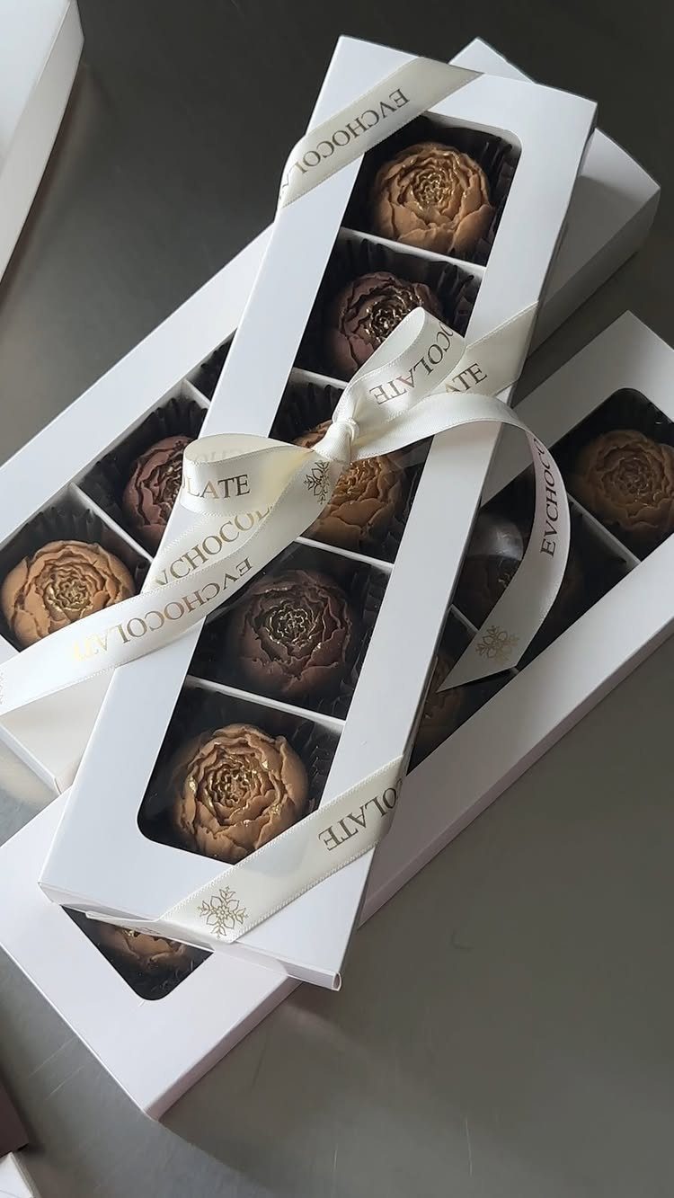 Artisanal rose-shaped chocolates in white gift boxes tied with a white ribbon.