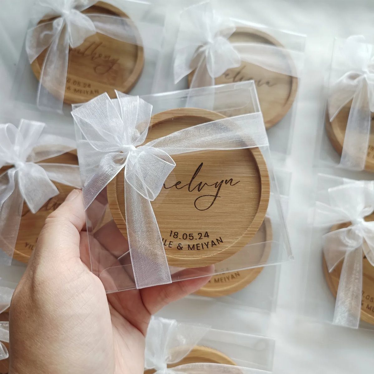 Round wooden engraved coasters wrapped in clear plastic with white sheer ribbons.