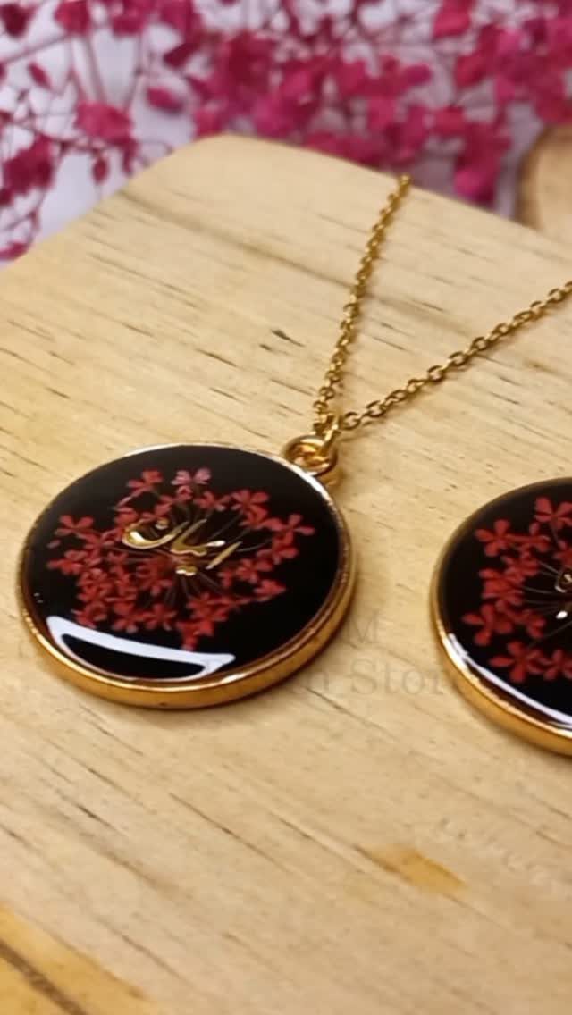 Gold necklace with a black circular pendant containing red flowers and calligraphy.