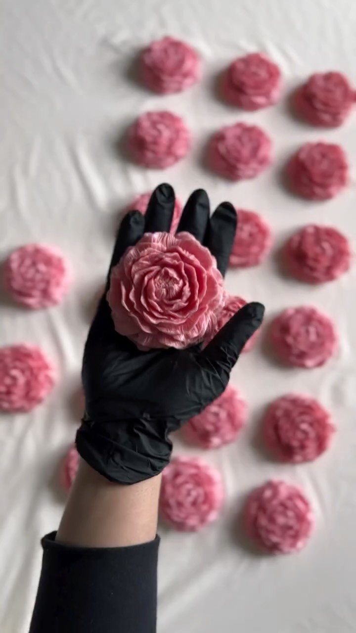 Pink rose-shaped handmade soaps held by a gloved hand on white fabric