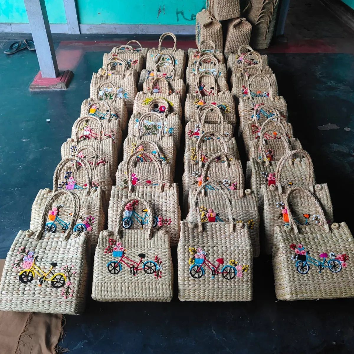 Woven straw handbags with colorful embroidered bicycle designs arranged in neat rows.