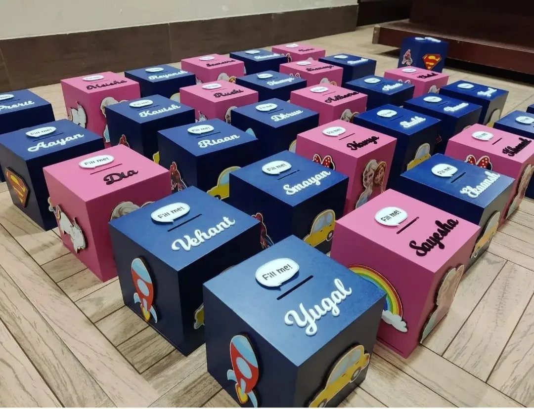 Personalized pink and navy blue cube piggy banks with names and colorful decorations.