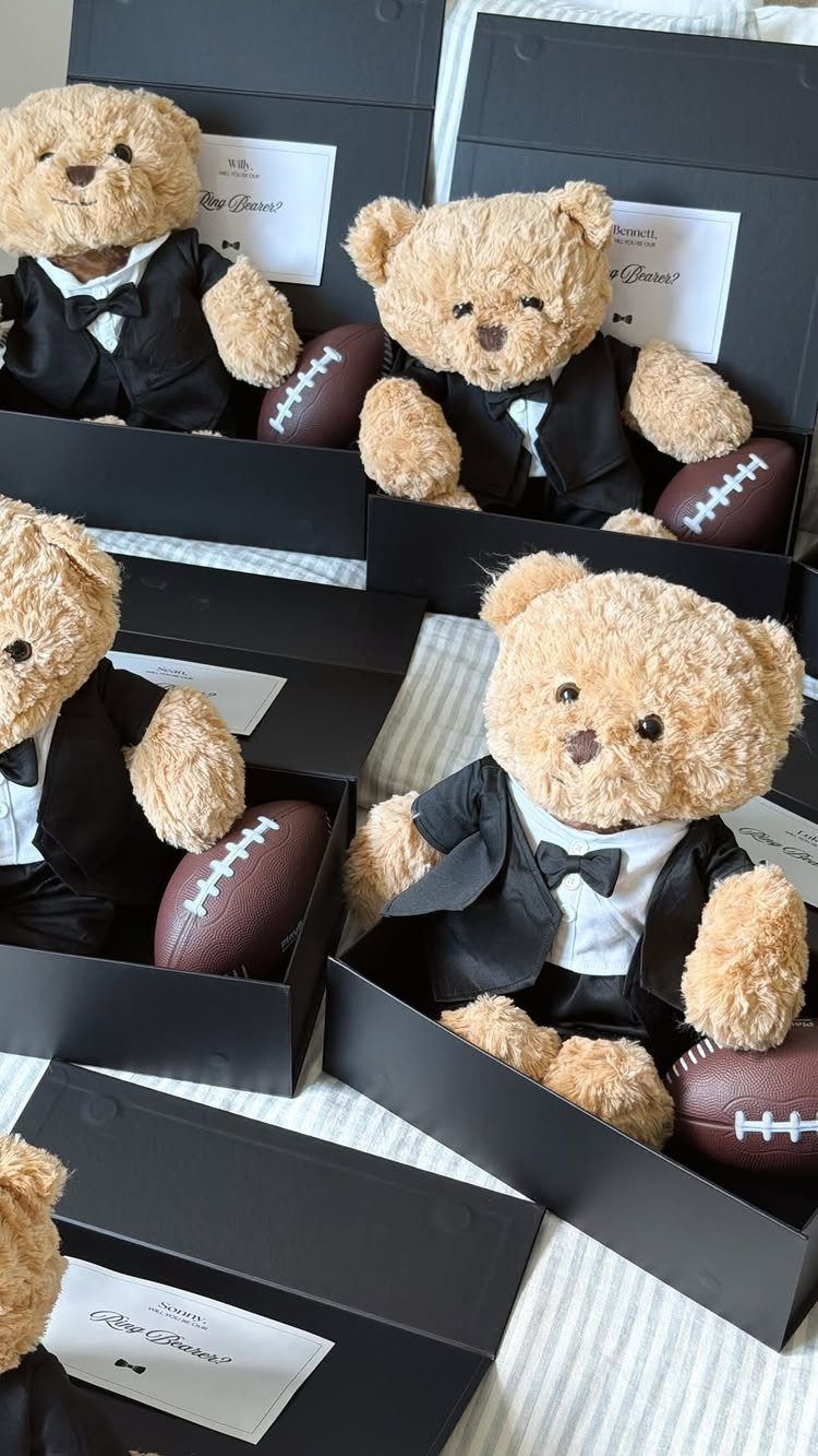 Teddy bears in tuxedos with footballs inside black gift boxes for ring bearers.