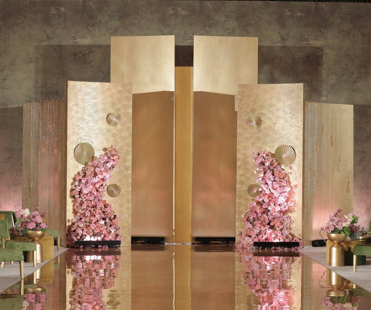Gold metallic event backdrop decorated with climbing pink roses and reflective flooring