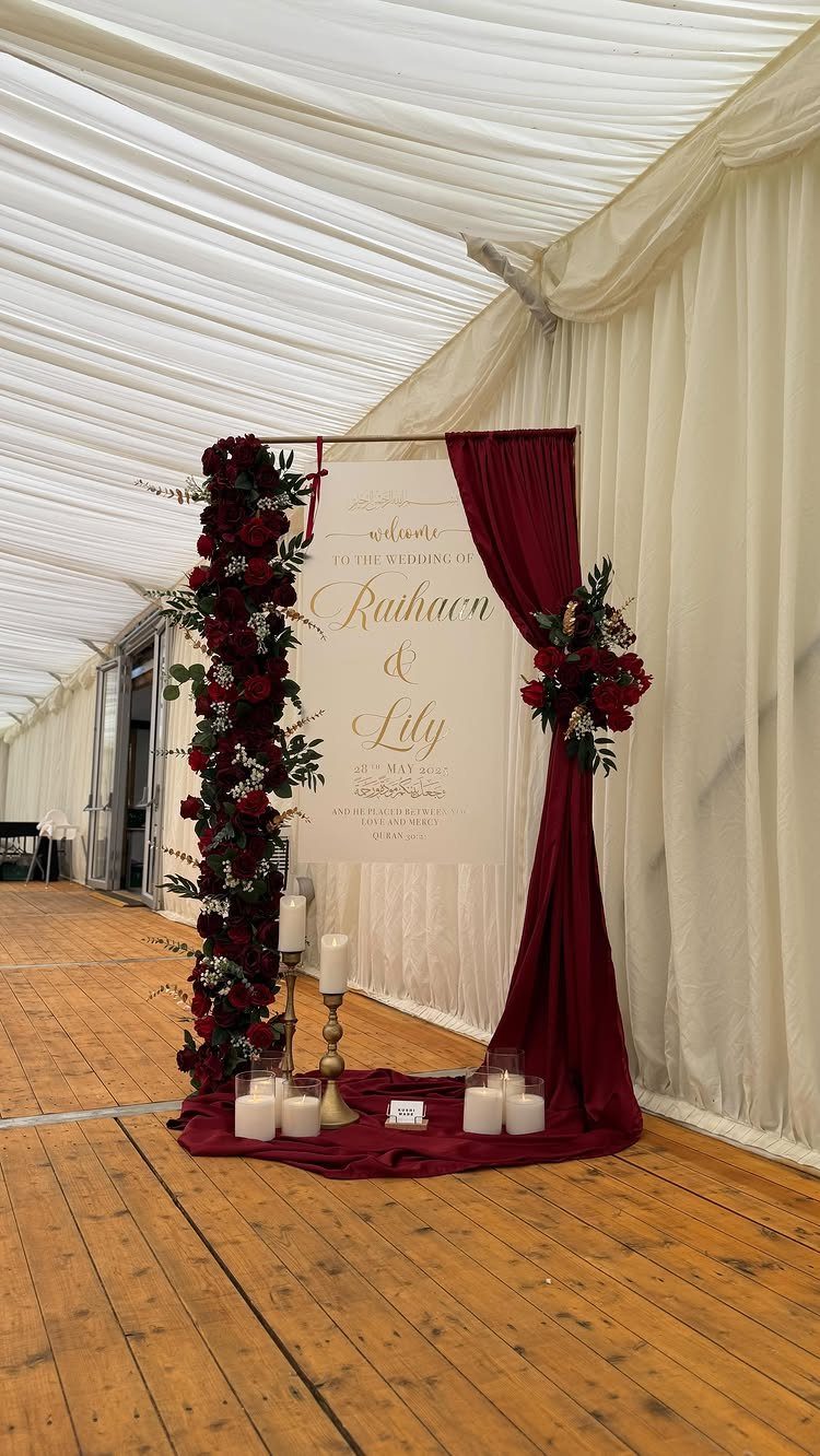 Wedding welcome sign framed by red roses and velvet curtains with gold candles.