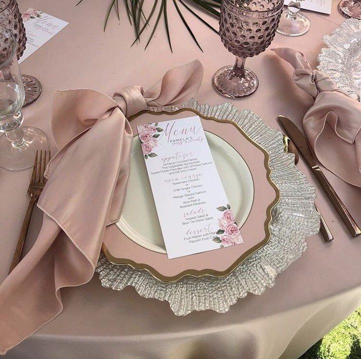 Wedding place setting with pink satin napkin, gold-rimmed plate, and floral menu card.