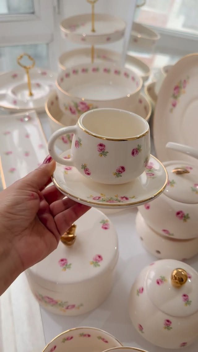 White ceramic teacup and saucer with pink roses and gold rims held by hand.