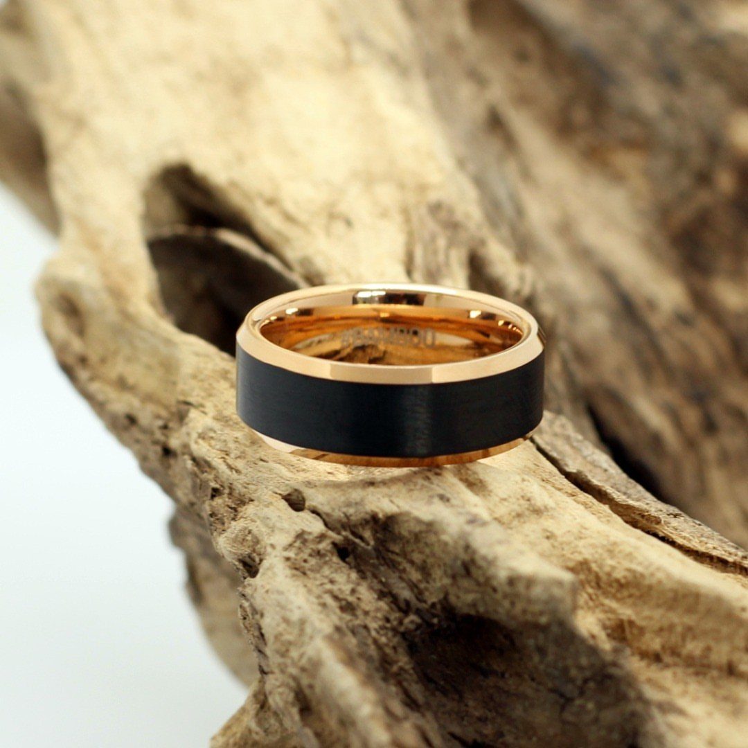 Rose gold and black band ring resting on a piece of weathered driftwood.