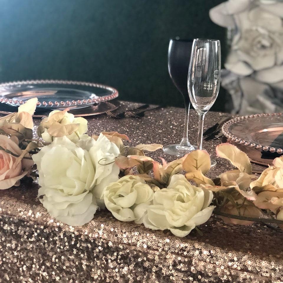 Rose gold sequin tablecloth with beaded plates, champagne glasses, and white roses.