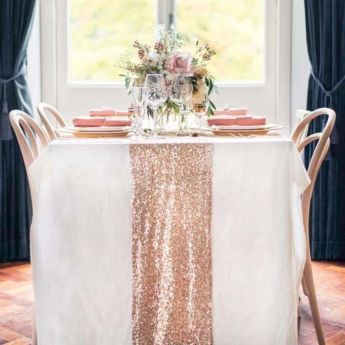 Wedding table with white cloth, rose gold sequin runner, and pink floral centerpiece.