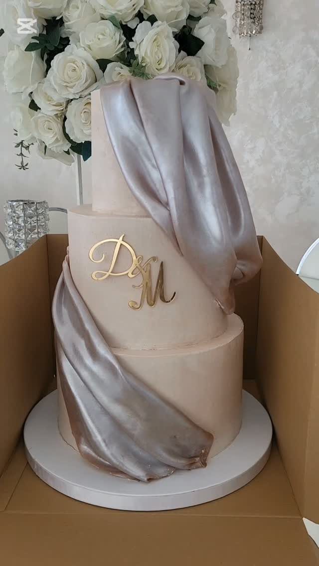 Three-tier rose gold wedding cake with metallic draping and gold initials D M.
