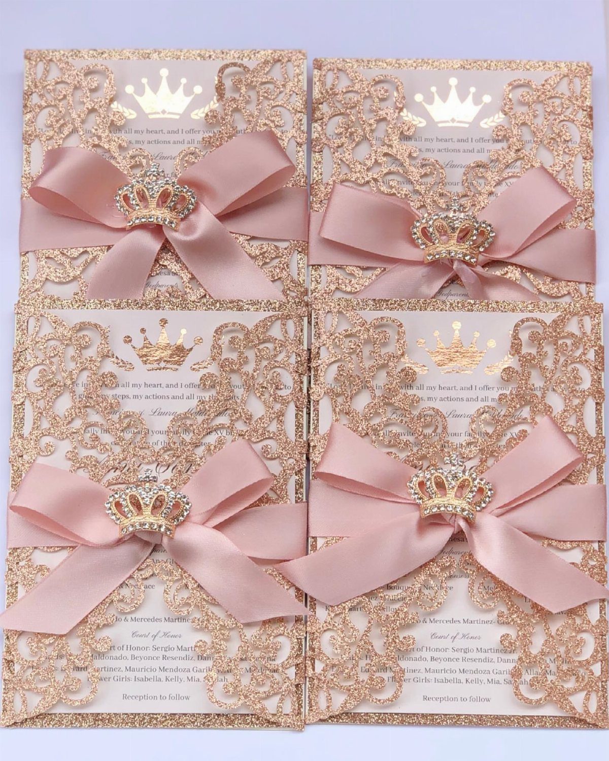 Rose gold wedding invitations with pink satin bows and jeweled crown accents.